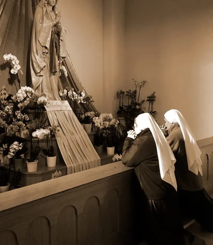 Irmãs do Instituto Hesed de joelhos, em oração diante de uma imagem de Nossa Senhora
